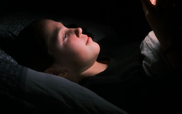 Mujer tumbada en la cama de noche, iluminada por la luz del móvil